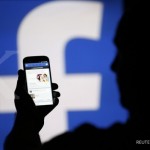 A man is silhouetted against a video screen with an Facebook logo as he poses with an Samsung S4 smartphone in this photo illustration taken in the central Bosnian town of Zenica